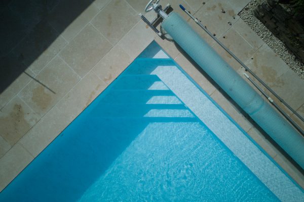 Close-up of the swimming pool steps and cover, with blue water and natural limestone surrounds.